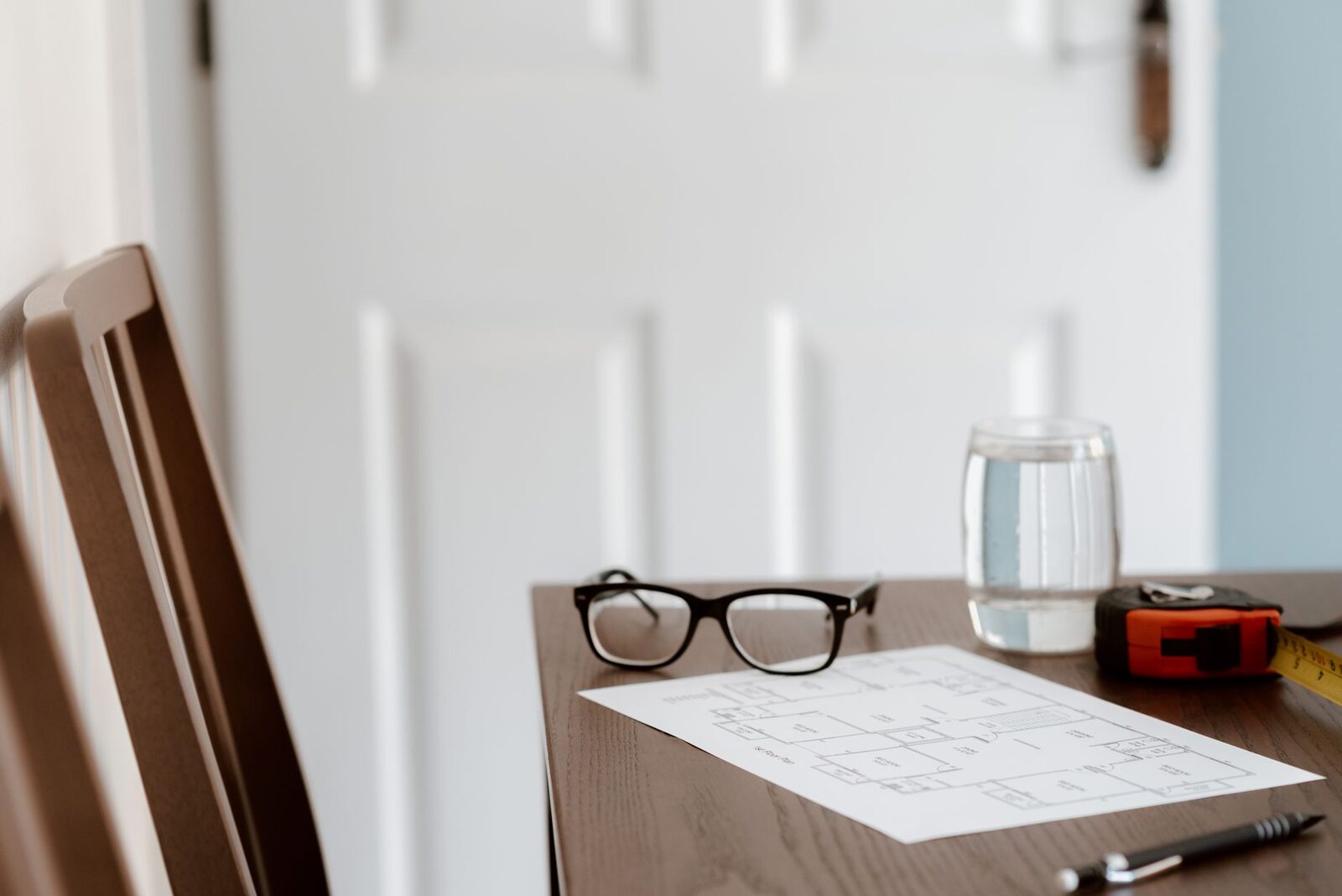 From above of desk with paper and pen with glasses and tape measure near glass of water in room in soft daylight